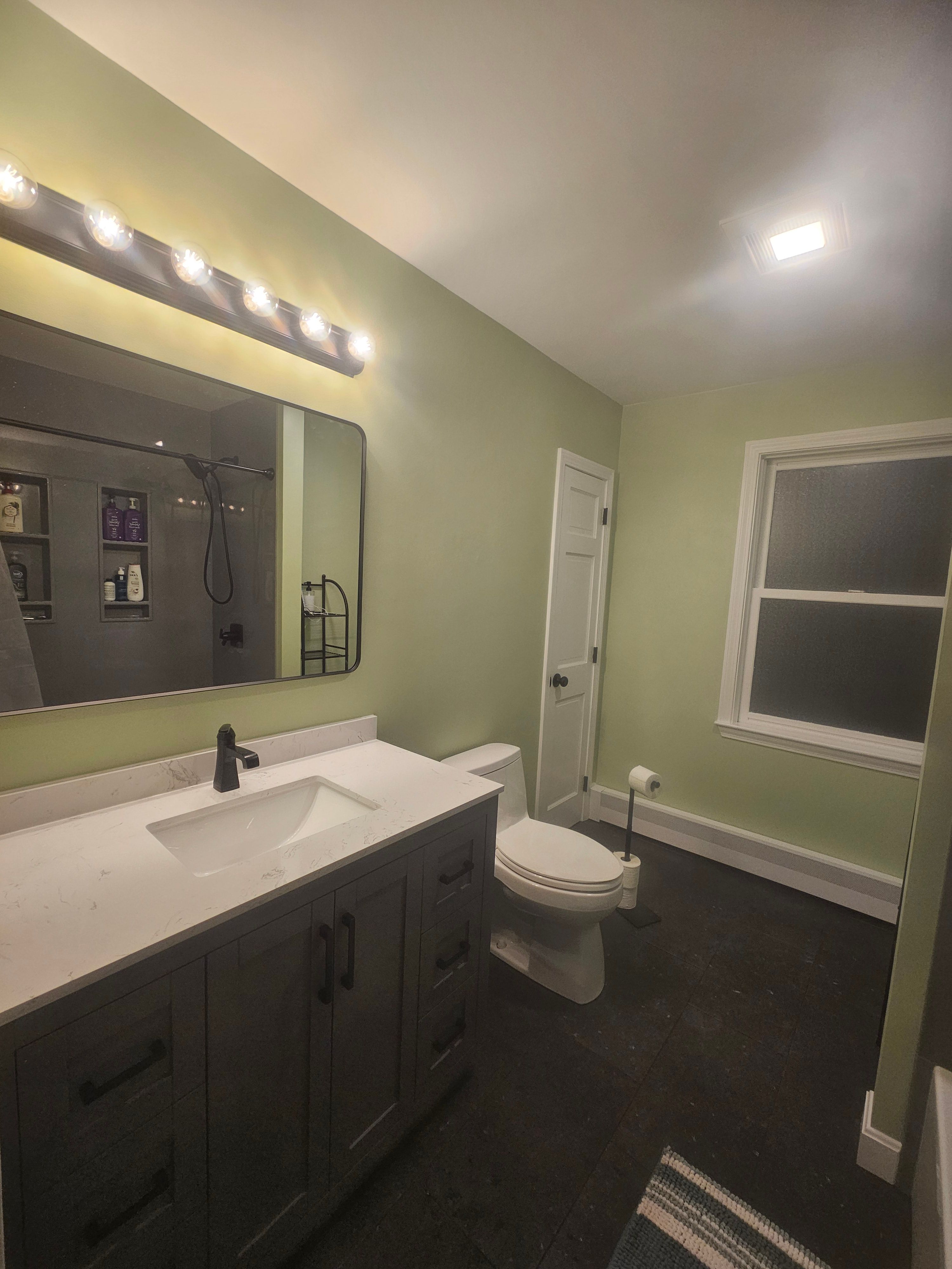 Beautifully remodeled bathroom with black fixtures and black porcelain tile, solid stone tub surround