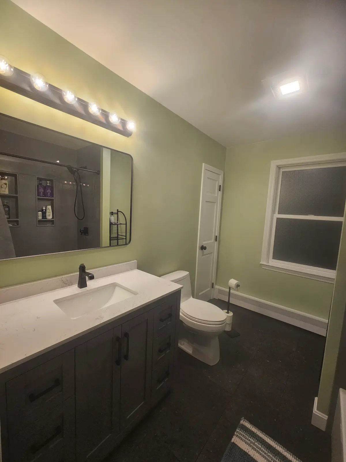 Beautifully remodeled bathroom with black fixtures and black porcelain tile, solid stone tub surround